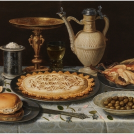 Mesa con mantel, salero, taza dorada, pastel, jarra, plato de porcelana con aceitunas y aves asadas